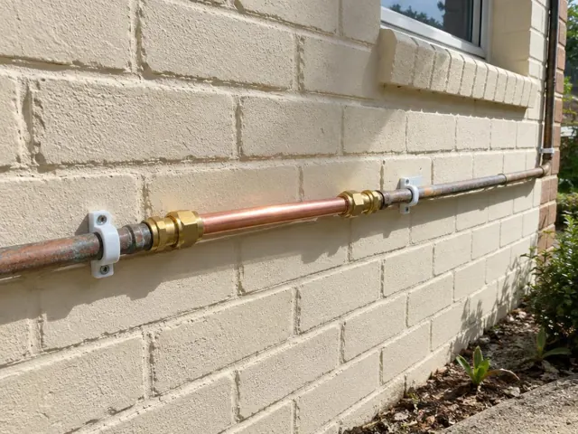 Copper water pipe repair on a cream brick exterior wall with wall clips in St Ives