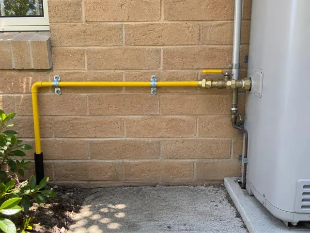 Yellow gas pipe and fittings on a brick exterior wall beside a hot water unit in Killara